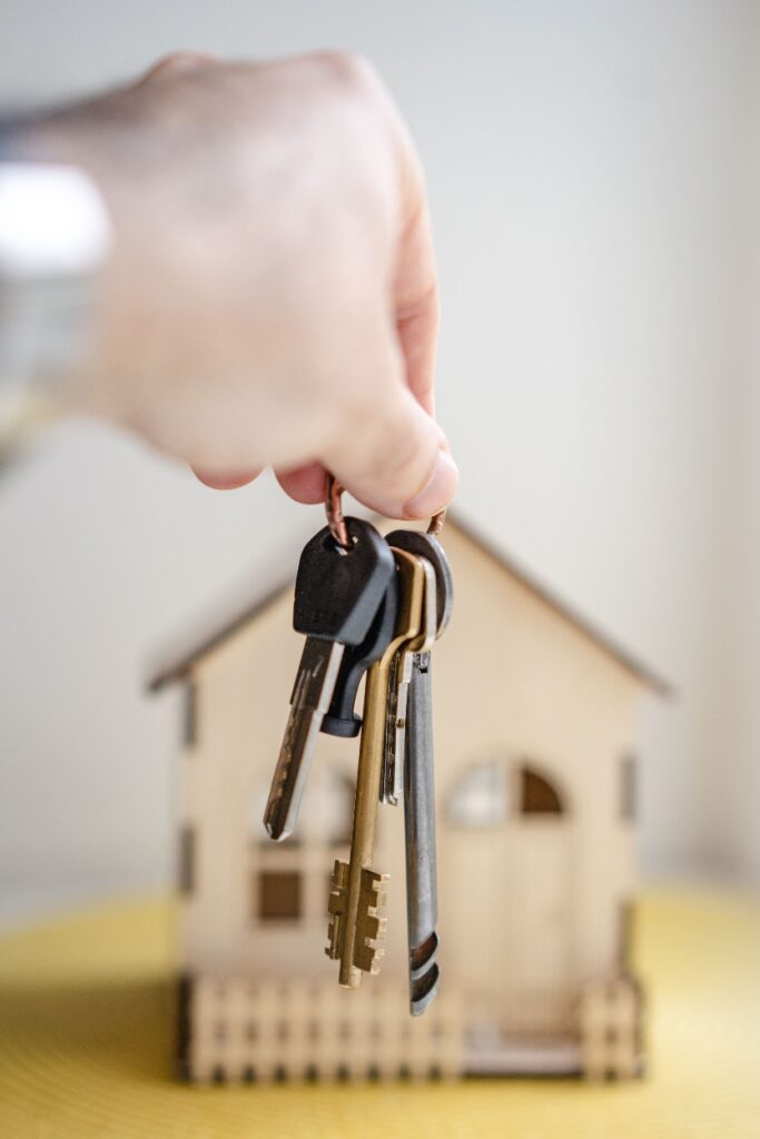A person holding keys in front of a model house. 