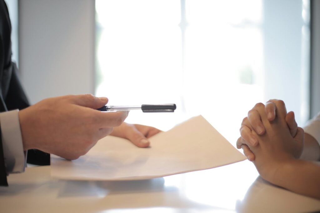 A person handing over a document and a pen to another person