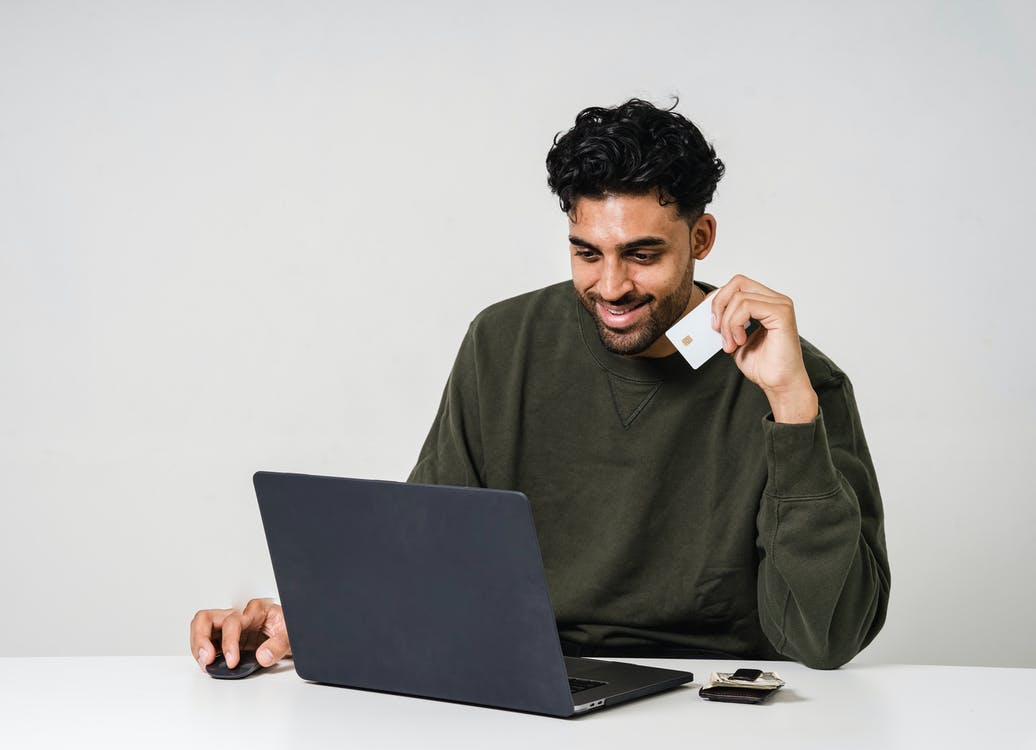 A man using a laptop with one hand and holding a credit card in his other hand
