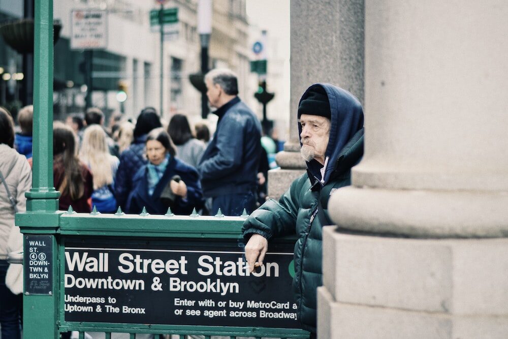 A man leaning against a Wall Street subway sign