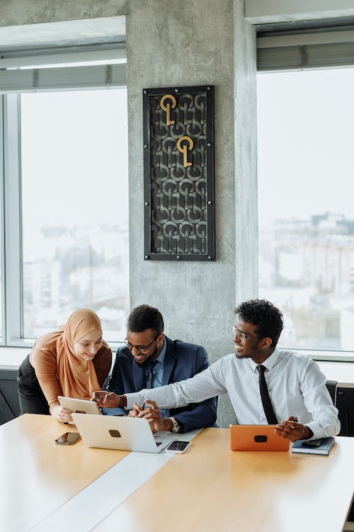 Three staff members engaged in a discussion at an office desk while using a tablet and laptops